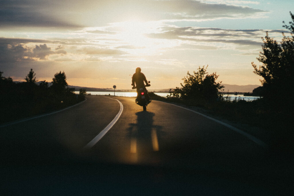 A person riding a motorcycle on a narrow Long Beach road during golden hour to represent motorcycle accidents compensated with help from lawyer for motorcycle accident
